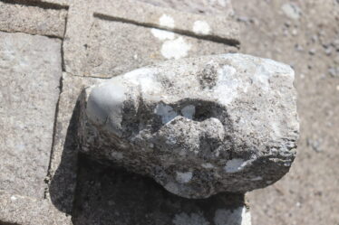 Head carving was once a corbel and now re-used on St. Kerrills 'bed' just inside the graveyard wall at the graveyard.