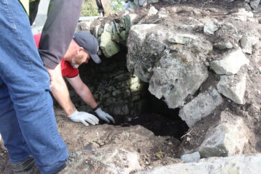 Man on his knees cleaning vault of tomb. Overseen by archaeologist | B. Doherty