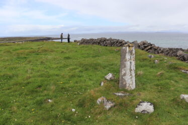 Standing stone with recumbant parts beside it in a green field with the sea visible in the distance