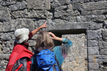 two people pointing and examining the wall over the lintel of the doorway of the stone built church | B. Doherty 2022