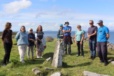 People standing at pillar stone, blue skey behind them and a glimpse of the sea | B. Doherty 2022
