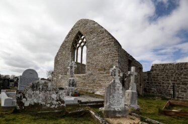 Arched tracery window within church ruin, recently conserved with grave