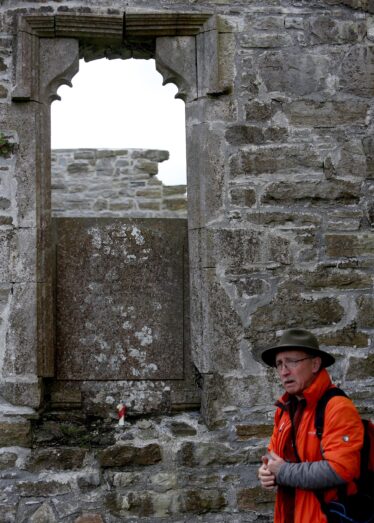 MAn in a hat talking about the inscribed wall plate on a stone wall