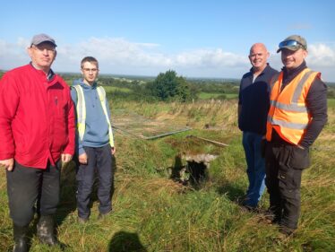 Four people standing in front of the entrance to a souterrain in a field.