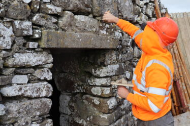 Man inbright orange safety gear and wearing a hard-hat repointing stonework above a lintel