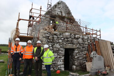 Three people stanfding in front of Kilcooley Church vault during works. Stone work is surrounded by scaffolding | B. Doherty 2025