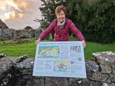 Peggy Monahan Standing behind Interpretive Sign at Kilboght