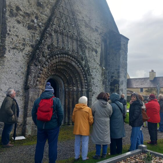 A group of people standing outside a Romanesque doorway as a man explains the history of it. | Lucy Flynn 2026