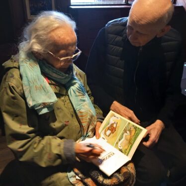 An elderly lady and elderly man sitting together reading a book between them.