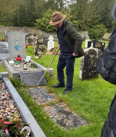 Man in had standing beside a grave-slab