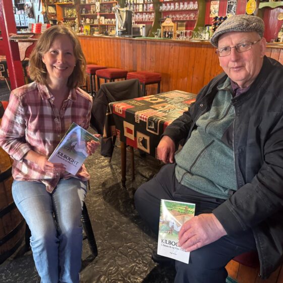 A man and a woman sitting side by side and holding up the book at a new book launch. | Lucy Flynn 2026