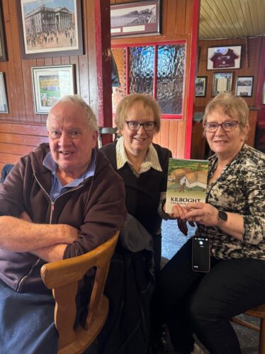 Two women and a man posing for a picture with a book at.