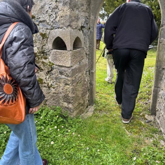 A picture of people walking through the doorway in Kilboght as they pass by the font built into the wall. | Lucy Flynn 2026