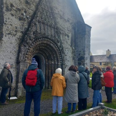 A group of people standing outside the decorated door of St. Brendan's Cathedral as a man explains the history
