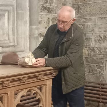 A man at a table holding a broken piece of a shrine at the table of an alter