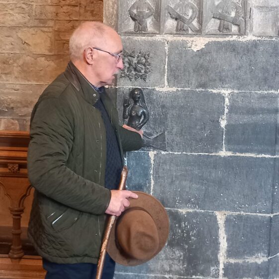A man standing by the wall in Clonfert Church as he explains the carving o the mermaid on the wall and tells us its story. | B. Doherty 2026