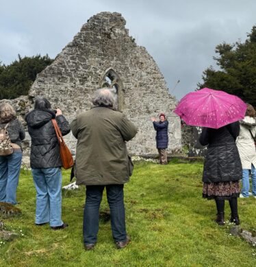 Group of people standing around the ruins of what is left of kilboght Church as a lady explains the history to the group.