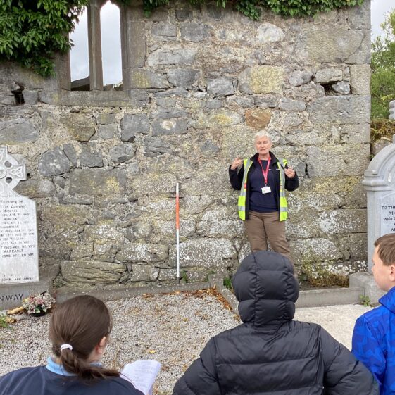 Person standing against a wall with children in front listening | Carmel O'Riordan