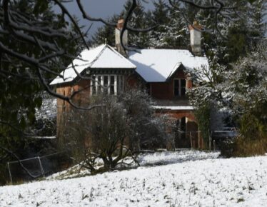 Red brick house with snow covering the roof and garden to the front