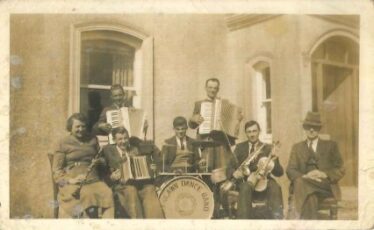 Group of musicians including a drummer, saxaphone player, fiddle player in front of Post office, Woodlawn