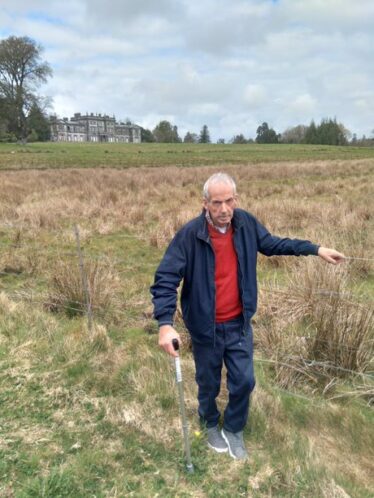 Man stands at fence with large house in background.