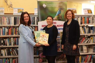 Three ladies standing with books in their hands in front of shelves of books