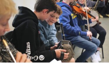 Boys playing instruments including box accordian, flute, whistle, violin